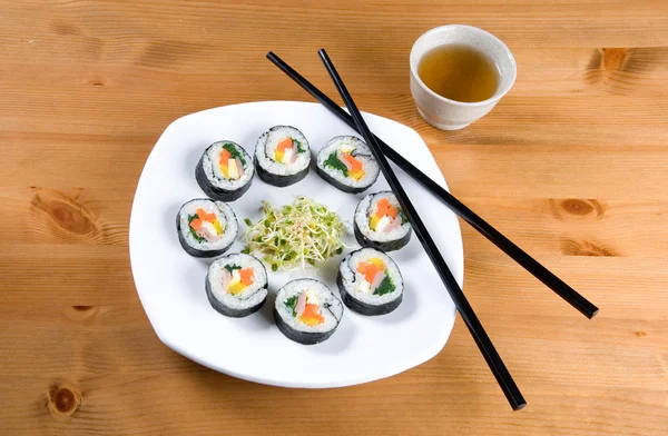 stock image A plate of Korean style sushi called kimbap and clover sprouts with a cup of tea.