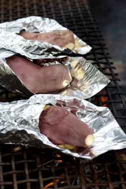 Sweet potatoes wrapped in aluminum foil are being cooked over an open fire. clipart