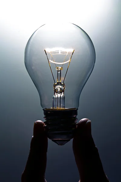 stock image A magically lit light bulb being hels by two fingers