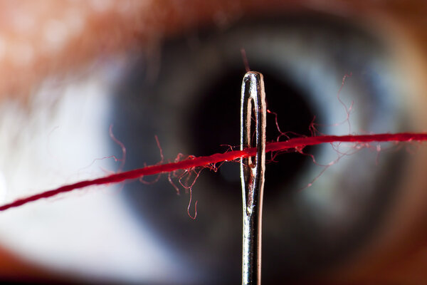 Threading of a cotton through the eye of a needle with eye in back ground