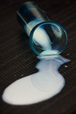 Milk spilled from an interest blue glass against a black background clipart