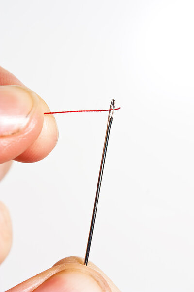 A needle being threaded with red cotton or thread