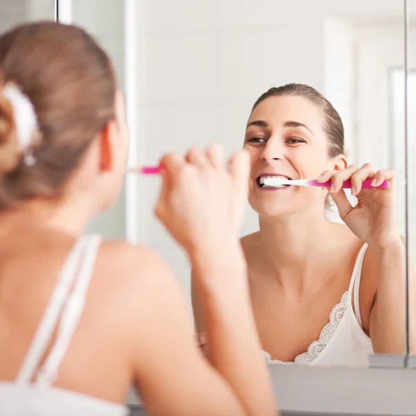 Mujer joven cepillándose los dientes en el lavabo — Foto de Stock