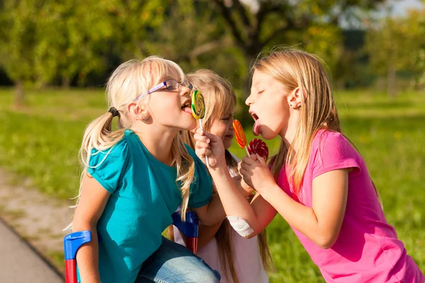 Três meninas comendo pirulitos, o — Fotografia de Stock