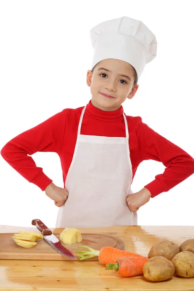 Smiling little chief-cooker on the desk with vegetables — Stock Photo, Image