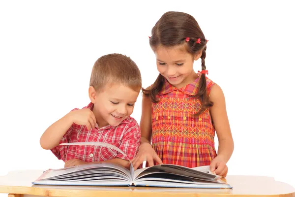Två leende barn läser boken på skrivbordet — Stockfoto
