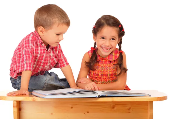 Двое улыбающихся детей читают книгу на столе — стоковое фото