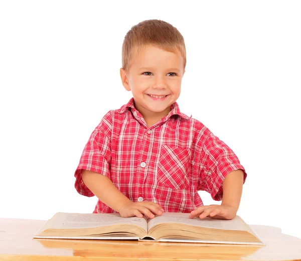 Smiling little boy reading book on the desk — Stock Photo, Image