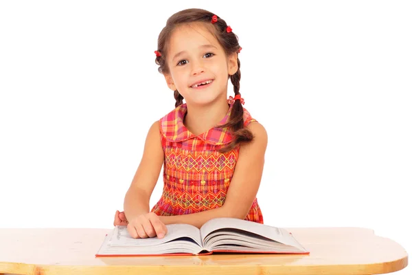 Smiling little girl reading book on the desk — Stock Photo, Image