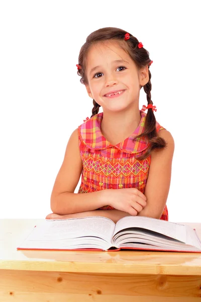 Lächelndes kleines Mädchen liest Buch auf dem Schreibtisch, — Stockfoto