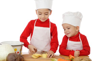 Smiling little chief-cookers on the desk with vegetables clipart