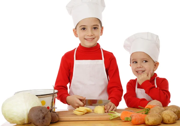 Lächelnde Kleine Chefkocher Auf Dem Schreibtisch Mit Gemüse Isoliert Auf — Stockfoto