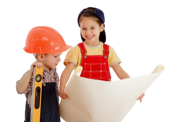Два улыбающихся маленьких строителя планируют с жидким уровнем и чертежом — стоковое фото