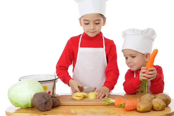 Smiling little chief-cookers on the desk with vegetables — Stock Photo, Image