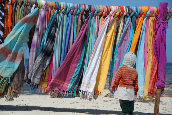 Verkaufsstand mit bunten Tüchern am Strand von Mombassa mit Kind im Vordergrund