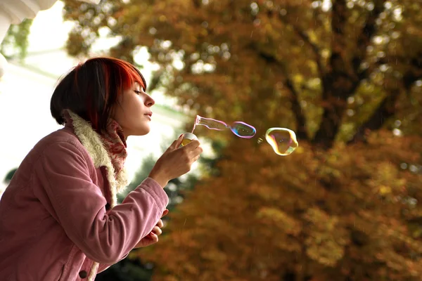 一个女孩的肖像是在秋天的公园吹肥皂泡 免版税图库图片