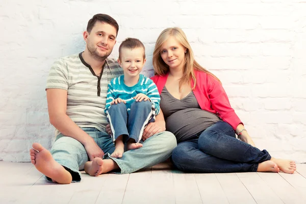 つの壁の近くの床に座っての幸せな家族 父および男の子 母親が妊娠しています — ストック写真