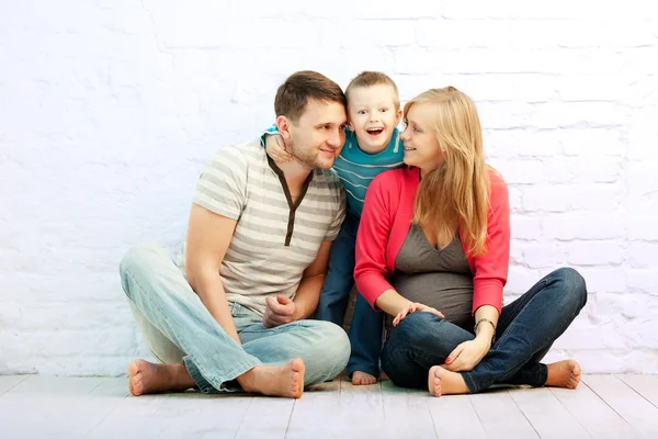 つの壁の近くの床に座っての幸せな家族 父および男の子 母親が妊娠しています 息子は疑問に思いました — ストック写真