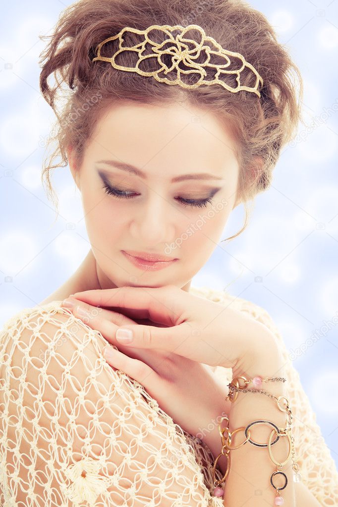 Young shy woman in a diadem and bracelets of gold on abstract background.