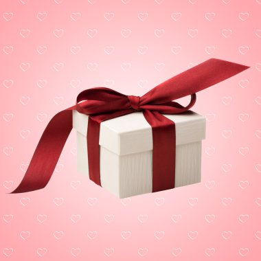 A white box tied with a red ribbon bow on pink abstract background with hearts. The best gift for Christmas, Birthday, Valentines's day or Wedding. clipart