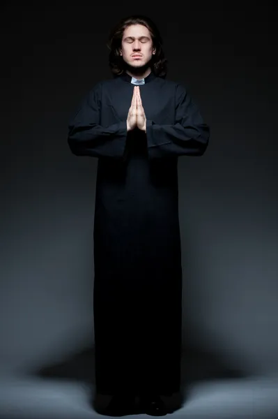 Young priest is praying against dark background — Stock Photo, Image