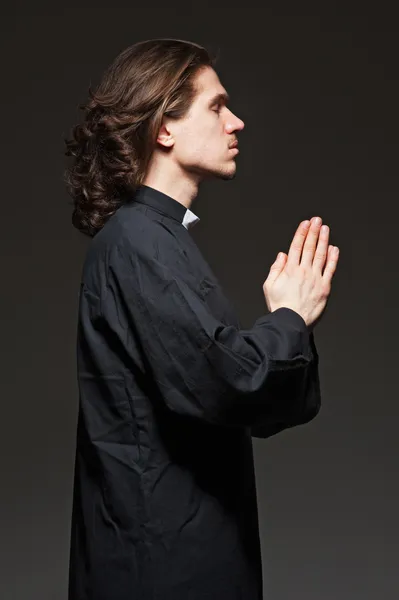 Jonge priester is bidden tegen donkere achtergrond — Stockfoto