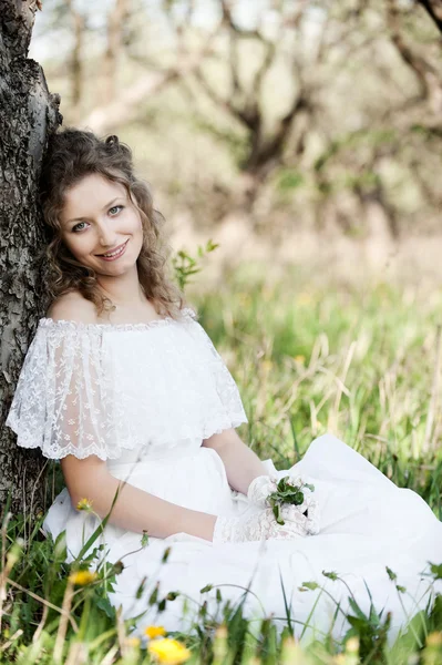 Красивая женщина в белом платье сидит на траве — стоковое фото