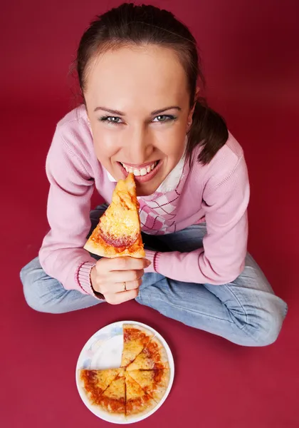 Красивая девушка сидит на полу и ест пиццу — стоковое фото
