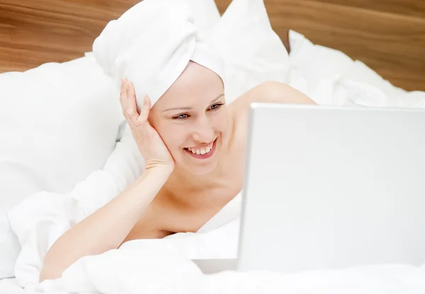 Smiley-Frau liegt mit Laptop im Bett — Stockfoto