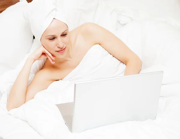 Женщина лежит на кровати и смотрит в ноутбук — стоковое фото