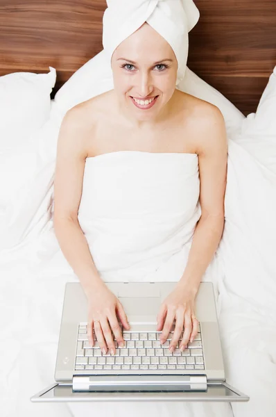 Jonge vrouw in bed met laptop na douche — Stockfoto