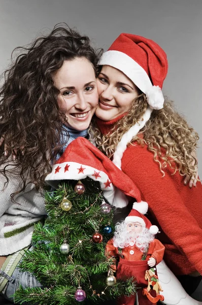 Двое улыбающихся друзей возле рождественской елки и Санты — стоковое фото