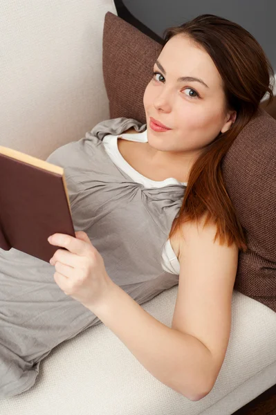 Mulher bonita com livro deitado no sofá — Fotografia de Stock