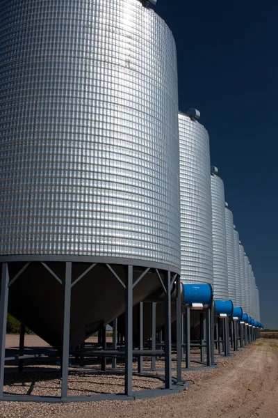 A row of shiny, steel grain silos in a field — Stock Photo, Image