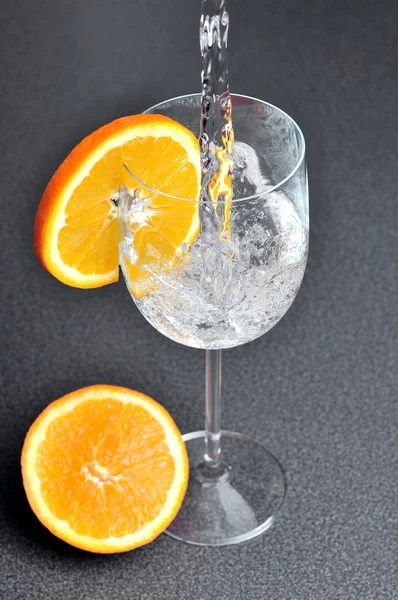 Наливание воды в стакан с апельсиновым ломтиком — стоковое фото