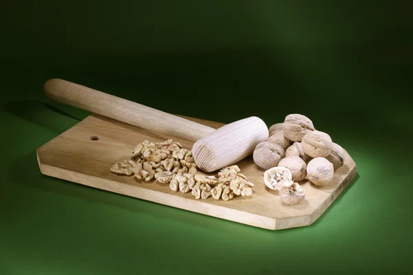 stock image Walnuts are split by a hammer on a darkly green background on a board