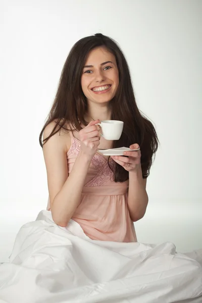 Lächelndes Mädchen im Bett mit einer Tasse Kaffee — Stockfoto