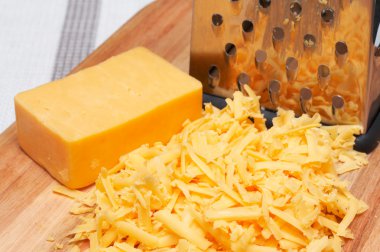 Grated cheddar cheese on wooden board clipart