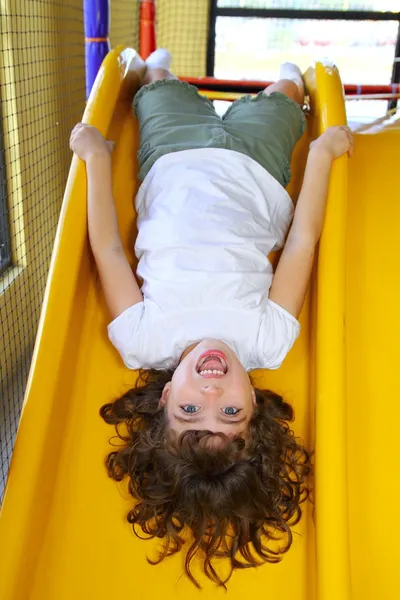 A l'envers petite fille sur aire de jeux toboggan riant — Photo