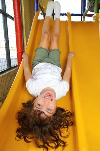 A l'envers petite fille sur aire de jeux toboggan riant — Photo