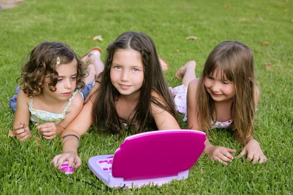 Tři malá holčička hraje s hračkou počítač v trávě — Stock fotografie