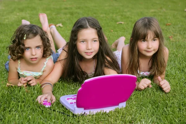 Три дівчинки грають з іграшковим комп'ютером у траві — стокове фото