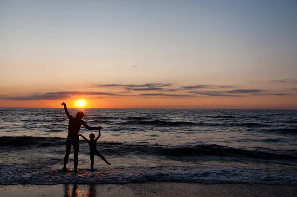 Silhuetas de pai e sua ducha na praia ao pôr do sol — Fotografia de Stock