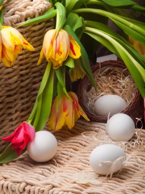 White eggs and spring tulips basket on straw tray