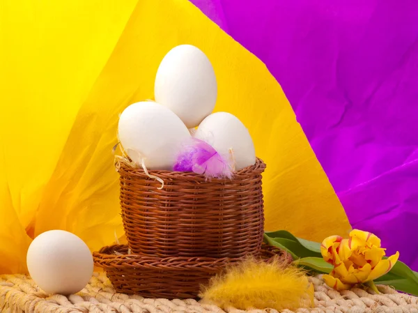 Ovos em cesta de palha com fundo amarelo e roxo — Fotografia de Stock