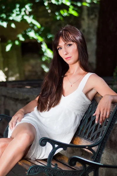 Giovane bella donna vestita di bianco sulla panchina — Foto Stock