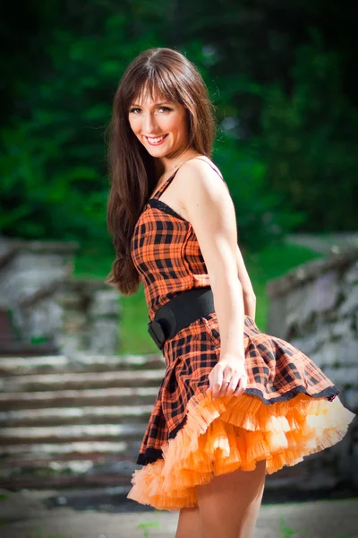 Mladá žena nosí oranžové šaty v parku — Stock fotografie