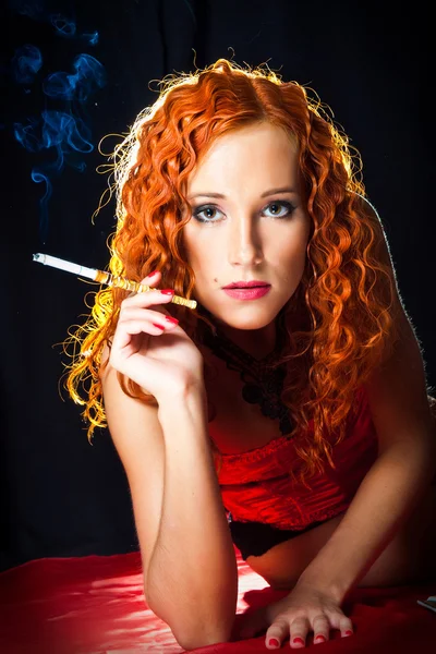 Sexy chica con el pelo rojo usando corsé rojo sosteniendo boquilla ámbar en blac — Foto de Stock
