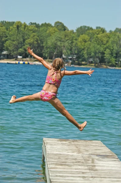 Mladá dívka skočí z doku se zbraněmi a roztaženýma nohama — Stock fotografie