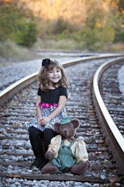 Little girl and teddy bear on railroad tracks clipart